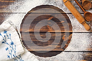 Flour scattered in the form of a circle, rolling pin and white linen napkin on an old wooden background. Place for text.