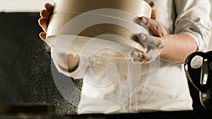 Flour sieve in male chef hands in the kitchen