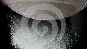 Flour is sifted through a sieve on black background