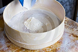 Flour is sifted through a wooden sieve