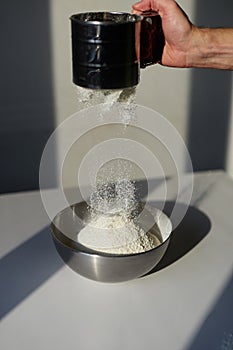 Flour sifting through metal sifter on white board