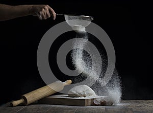 Flour is sprinkled over a ball of dough on a wooden board with r