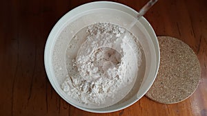 Flour,tremors, salt, sugar, water in a white bowl on a wooden table. Cooking process. Pancakes recipe.