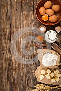 Flour in a wooden bowl on dark wooden background with spikelets of wheat, eggs, milk and butter, ingredients for bakery products,