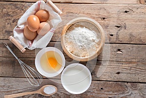 The flour in a wooden bowl, egg, milk and whip for beating.