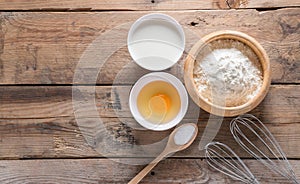 The flour in a wooden bowl, egg, milk and whip for beating.