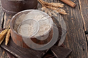 Flour in a wooden bowl with sieve on vintage board