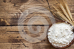 Flour in wooden bowl and wheat ears on wooden background. Copy space