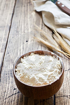 Flour in wooden bowl and wheat ears on wooden background. Copy space