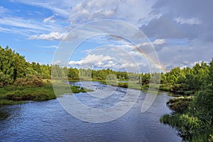 The flow of Kasmanjoki river bordered by pin forests in Finnish Lapland. The sky with rainbow is at background. Picture is taken