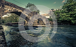 Flow of a river under the Abergorlech arched stone bridge surrounded by trees