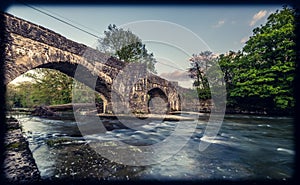 Flow of a river under the Abergorlech arched stone bridge surrounded by trees