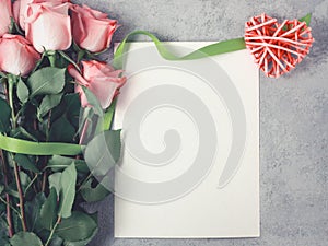 Flower arrangement - a bouquet of pink roses, a wicker heart and an empty sheet for inscription on a concrete surface