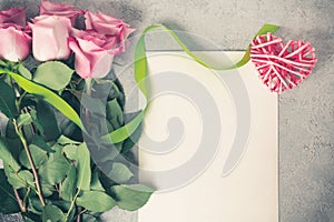 Flower arrangement - a bouquet of pink roses, a wicker heart and an empty sheet for inscription on a concrete surface