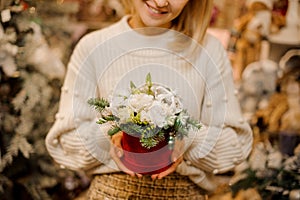 Flower arrangement in box of white flowers with fir branches and christmas toys in woman`s hands