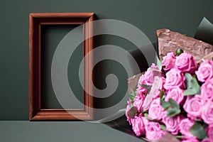 Flower arrangement. Pink flowers, wooden brown photo frame on pastel green background, copy space