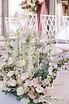 Flower arrangement of pink roses, buttercups and white bells and eucalyptus near the transparent chairs