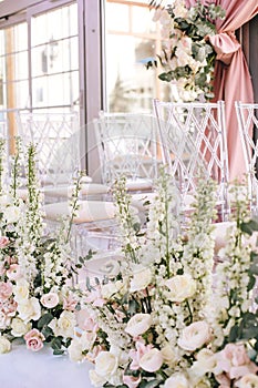 Flower arrangement of pink roses, buttercups and white bells and eucalyptus near the transparent chairs