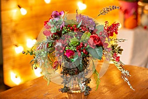 Flower arrangement with red berries, red roses and greens on the table