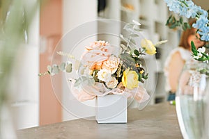 Flower arrangement with yellow and pink roses and eucalyptus in gift box on table in the flower shop, modern floristic