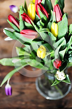 Flower background: bouquet of colorful tulips in a glass vase on a natural wooden background, postcard, mocap for mother