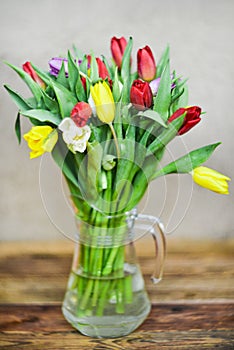 Flower background: bouquet of colorful tulips in a glass vase on a natural wooden background, postcard, mocap for mother