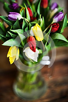 Flower background: bouquet of colorful tulips in a glass vase on a natural wooden background, postcard, mocap for mother