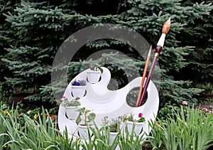 Flower bed in the form of an artist`s palette with a pencil and a brush for drawing