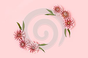 Flower border frame made of dahlia and green leaves on a pink pastel background.