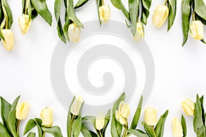 Flower border frame made of yellow and beige buds tulip on a white background. The apartment lay, top view. Floral