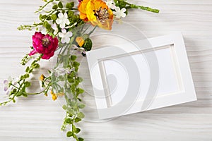 Flower bouquet and a blank white photo frame, copy space, on a white wooden background.