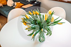 Flower bouquet from yellow tulips in vase on white table background In a living room. Closeup.