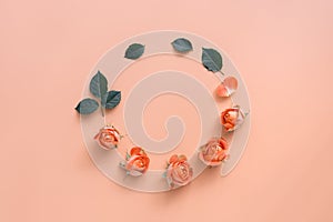 Flower composition, round frame of delicate coral heads of roses and green leaves on a pastel pink background. Flat lay, top view