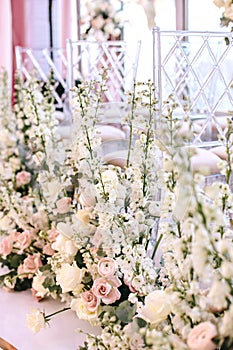 Flower compositions of roses, buttercups and white bells near transparent chairs at the wedding ceremony