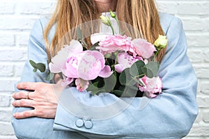 Flower delivery concept of packing flowers. The girl holds pink peonies, against the background of a white brick wall