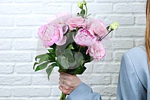 Flower delivery concept of packing flowers. The girl holds pink peonies, against the background of a white brick wall