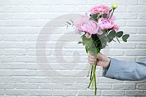 Flower delivery concept of packing flowers. The girl holds pink peonies, against the background of a white brick wall