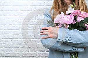 Flower delivery concept of packing flowers. The girl holds pink peonies, against the background of a white brick wall