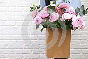 Flower delivery concept of packing flowers. The girl holds pink peonies in a craft bag, against the background of a