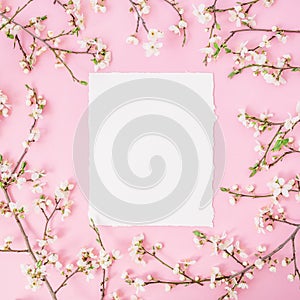 Flower frame with white flowers and paper vintage card on pink background. Flat lay, top view.