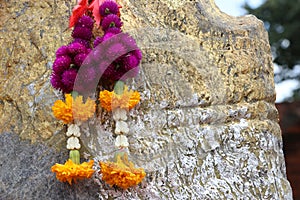 Flower garland of purple globe amaranth with yellow marigold and crown flower hanging on rock.