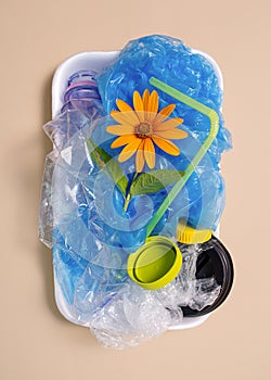 A flower in a plastic container with garbage on a beige background. The concept of environmental pollution. Land pollution