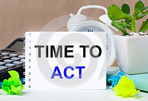 Flower in a pot, calculator, white alarm clock, multi-colored pieces of paper and a white notebook with the text TIME TO ACT on