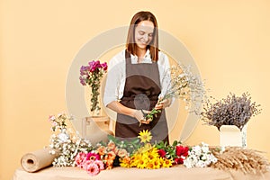 Flower shop ambiance. Workplace floral arrangements. Fresh blossoms for sale. Smiling woman florist in brown apron making bouquet