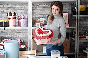 Flower shop: a florist girl demonstrates a large heart-shaped bouquet of red and white roses assembled in the workshop
