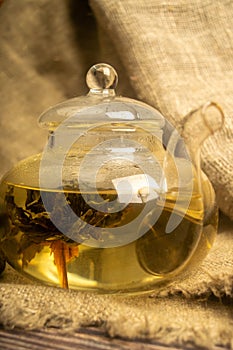 Flower tea brewed in a glass teapot on a background of homespun fabric with a rough texture. Close up