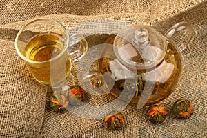 Flower tea brewed in a glass teapot, a glass of tea and balls of flower tea on a background of rough homespun fabric. Close up
