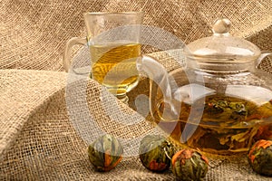 Flower tea brewed in a glass teapot, a glass of tea and balls of flower tea on a background of rough homespun fabric. Close up