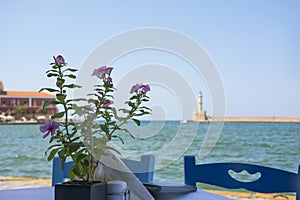 Flower and view from the cafe to sea and Venetian Harbor with lighthouse of Chania Old Town. Crete island of Greece