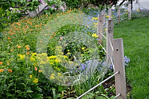 Flowerbed with colorful perennials and wooden fence posts with ropes in the park